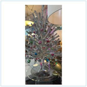 Vintage 6-foot silver aluminum Christmas tree decorated with colorful glass ornaments.